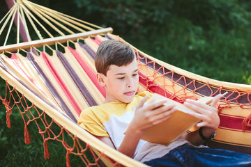 boy reads a book while lying in a hammock outdoors