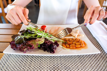 Woman having healthy breakfast, green salad with grilled chicken breast, chili bologna and baked beans