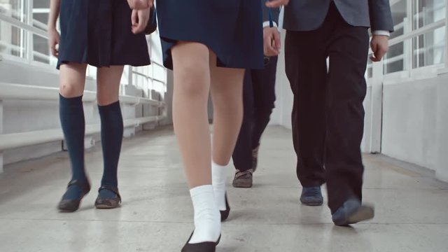 Low section of legs of little schoolgirls wearing uniform skirts with knee-high socks walking along hallway with schoolboys in twill pants heading to lessons