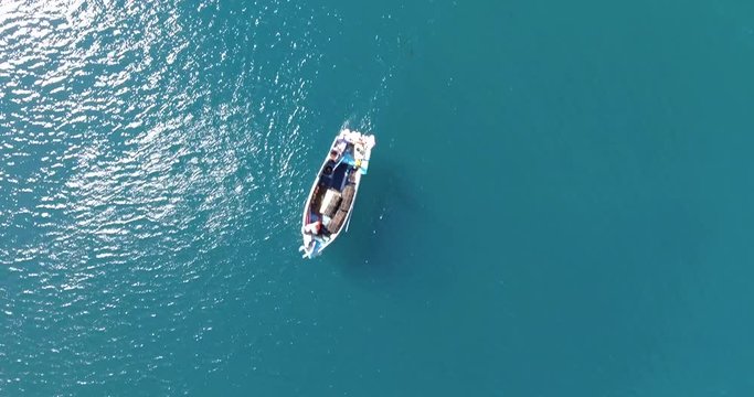 Aerial view looing down onto a turquoise sea with a small fishing boat sailing through