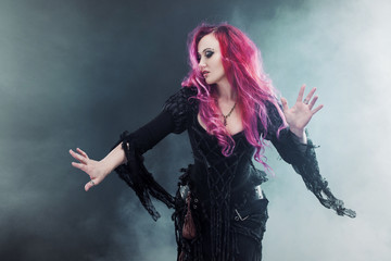 Halloween Witch creates magic. Attractive woman with red hair in witches costume standing outstretched arms, strong wind