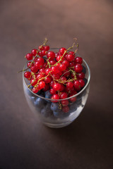 A glass full of tasty blueberries and red currants on a brown ba