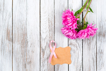 Pink breast cancer ribbon and pink flowers on wooden background.
