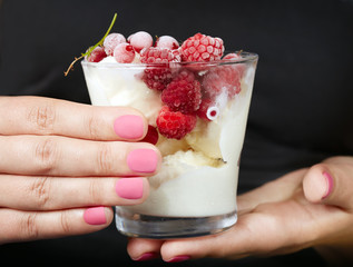 Hands with pink matte manicured nails holding a jar with ice cream and berries
