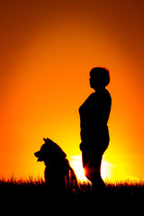 Silhouette of woman with dog on the beach, sunset background