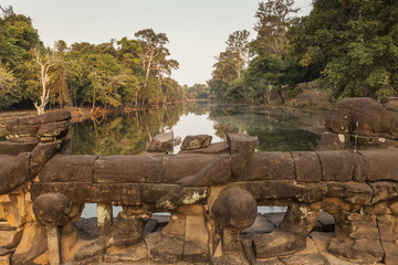 Headless statues on the bridge to one of the four entrance gates at Preah Khan temple, Angkor, Cambodia. Sunset light background