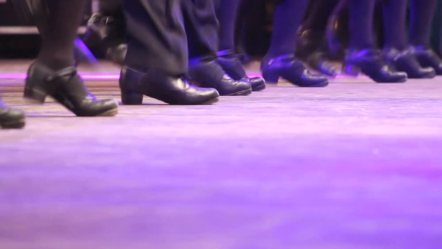 One row of people doing Irish dance with traditional step shoes. Close up single line of dancing feet on stage. Music, tradition and culture of Ireland. Celtic show on wooden floor