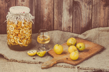 Jar of liquor with quince fruits on a wooden table 