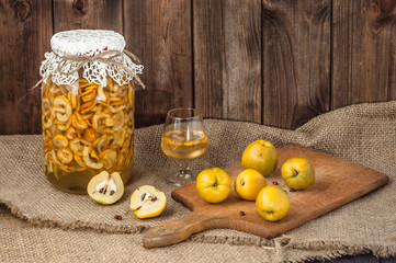 Quince tincture in a glass jar and fresh quince fruits on a wooden table