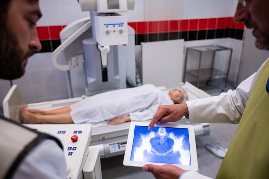 Doctors examining x-ray on digital tablet with patient in background
