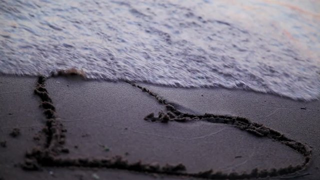 Heart drawn jn beach sand washed away by waves