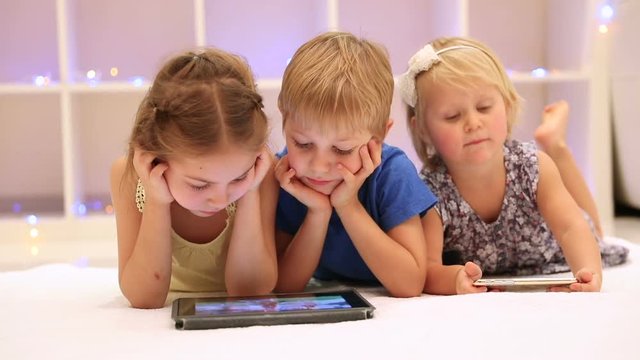 Three cute little child lying down on the floor in playing room and watching animated cartoons on the tablet, happy loving siblings spending time together. Full HD Video 1920x1080