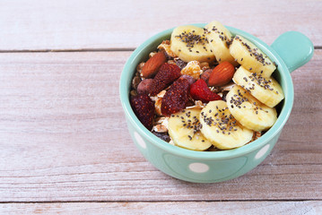 Top view of a bowl of Muesli with dried fruit, nuts and bananas on a wooden table.