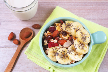 Top view of a bowl of Muesli with dried fruit, nuts and bananas on a wooden table.
