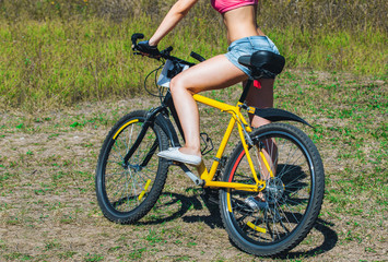 Fototapeta na wymiar Girl athlete in jeans, short shorts riding a bike in the park.