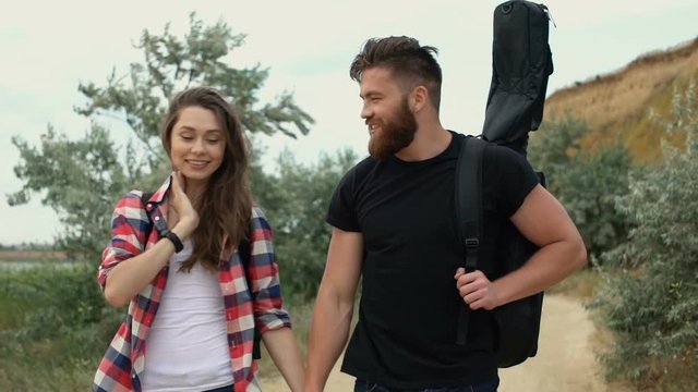 Beautiful young smiling couple with backpack walking along the road and holding hands 