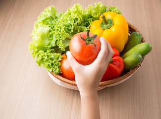 Tomato on hand with fresh vegetable prepared in bowl on wooden table