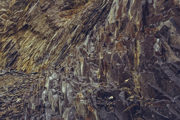 Arid strata volcanic rock cliff and stone debris in an old abandoned basalt quarry near the Racos extinct volcano in Brasov county, Romania.