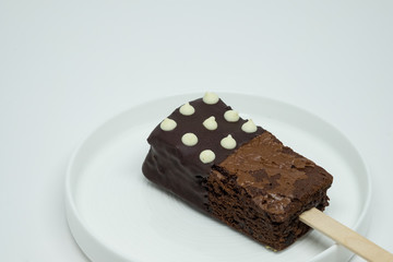 Decorative brownie with stick on the white plate.