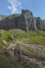 Picturesque mountain landscape with green alpine grasslands, dry riverbed and steep rocky cliffs in the vast Malaiesti Valley in Bucegi mountains, Romania. Romanian travel destinations.