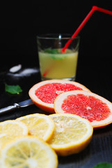 slices of grapefruit and lemon, a mint leaf and glass of juice on a black table. close up image...