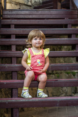 Charming little girl baby sitting on the wooden stairs in a beautiful dress while walking in Lviv