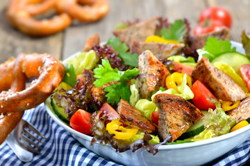 Bayerische Salatschüssel: Gebratene Milzwurst auf buntem Salat mit Breze serviert - Bavarian salad: Fried sausage with pieces of spleen served on a colorful salad