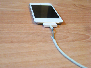 Broken old charger cable with white smart phone isolated on wooden table background