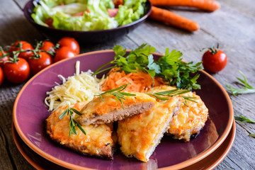Fototapeta na wymiar Baked pork cutlets coated in cheese and carrot with salad