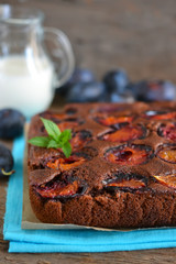 Chocolate cake with plums on a dark background with milk and min