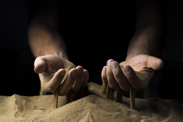 pours sand from his hands on a black background