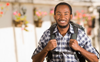 Young happy man wearing casual clothes and backpack posing for camera, smiling, garden environment, backpacker concept