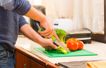 Closeup hands of man wearing blue sweater chopping vegetables on kitchen table