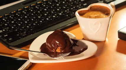 Cup of coffee and chocolate cake next to computer.