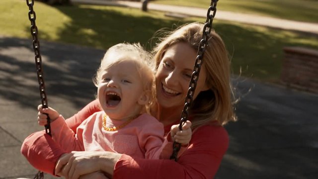 Mother and little girl on swing in playground