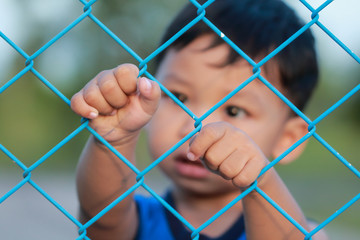 The boy standing of  pulling a metal fence .