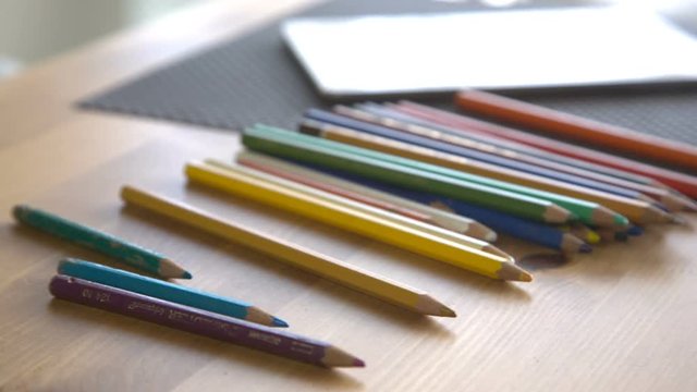 It is close-up image of woman putting colorful pencils on table