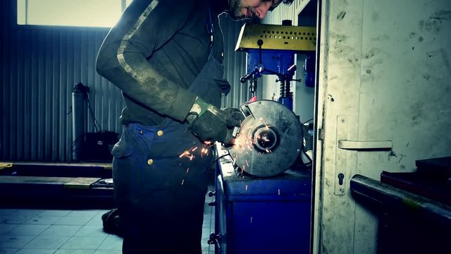 Mechanic polish steel parts and sparks coming from grinder tool. Zoom out.