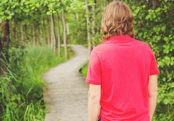 Young man, wearing red shirt, walking in a park on the trail.