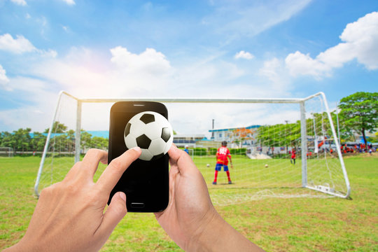 Man use mobile with football on screenshot , blur image of soccer field background.
