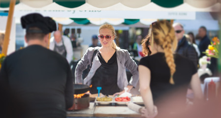 Beautiful blonde caucasian lady buying freshly prepared meal at a local street food festival. Urban international kitchen event in Ljubljana, Slovenia, in summertime.