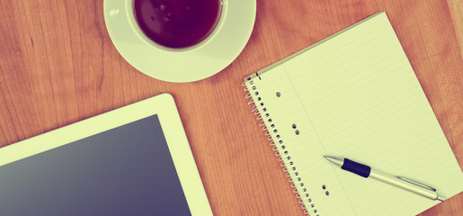 tablet PC and notepad and a cup of tea on wooden table from abov