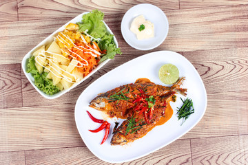 Mackerel fish fried topped spicy curry served with salad on wood.