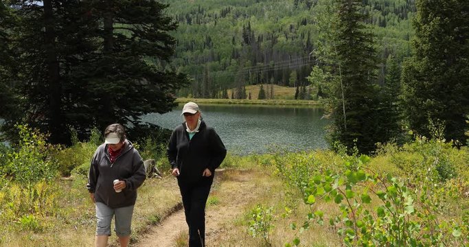 Two women hike mountain lake trail. Beautiful clear water mountain lake. Nature in natural environment. Recreation, hiking, and fishing ponds. Potter's Pond. Campground destination.