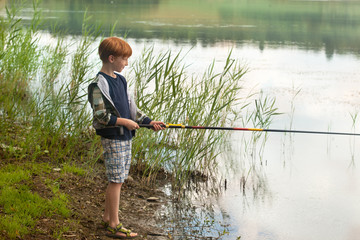 Little boy with fishing rod on a lake shore