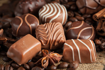 Assortment of dark, white and milk chocolate stack, chips. Chocolate and coffee beans on rustic wooden sacking background. Spices, cinnamon. Selective macro focus. Chocolates background. Sweets