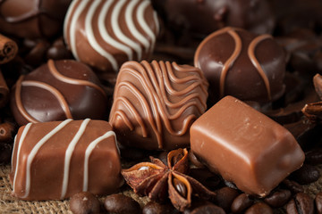 Assortment of dark, white and milk chocolate stack, chips. Chocolate and coffee beans on rustic wooden sacking background. Spices, cinnamon. Selective macro focus. Chocolates background. Sweets