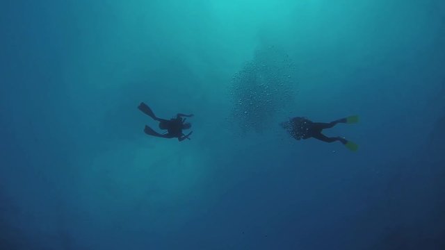 Divers swim underwater in wetsuit with aqualungs in flippers. Blue clean ocean. Deepness.