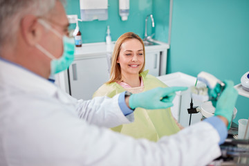 Fototapeta premium Woman in dental chair look at jaw model in dentist hands
