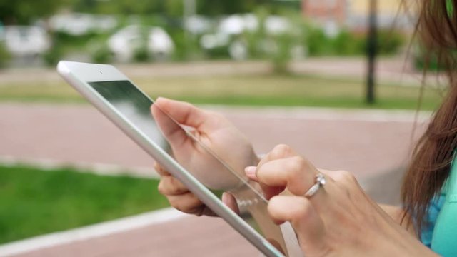 Women's hands with the mini white tablet. Uncertain woman uses a touchscreen